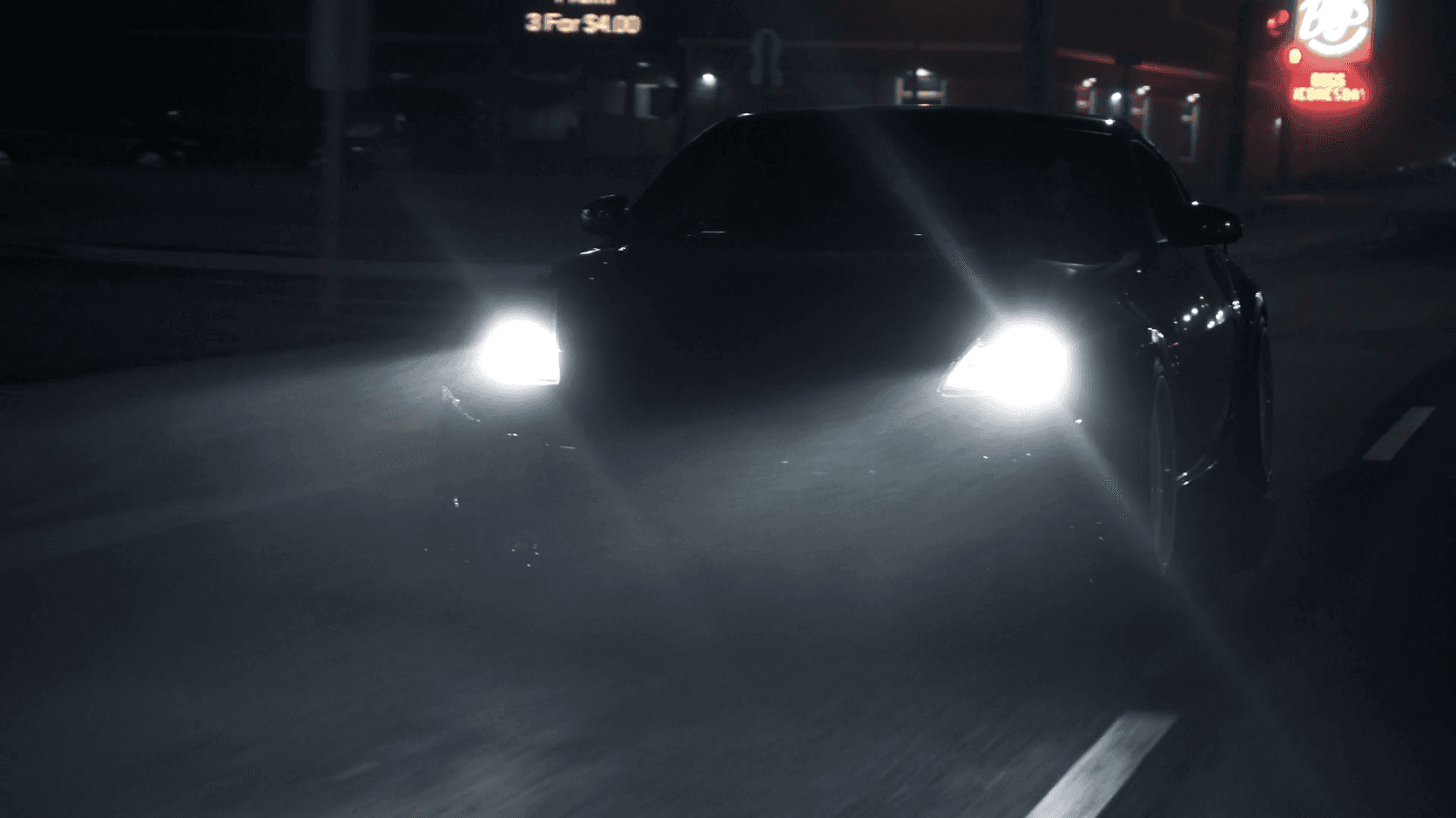 Black sedan with its headlights on, arriving at night