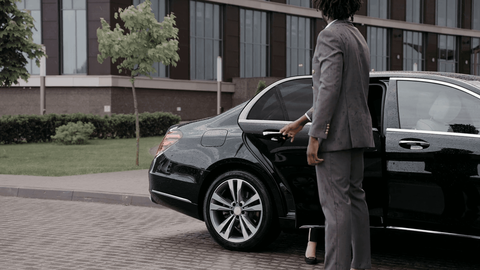 Chauffeur in a grey suit opening the rear door of a black executive sedan